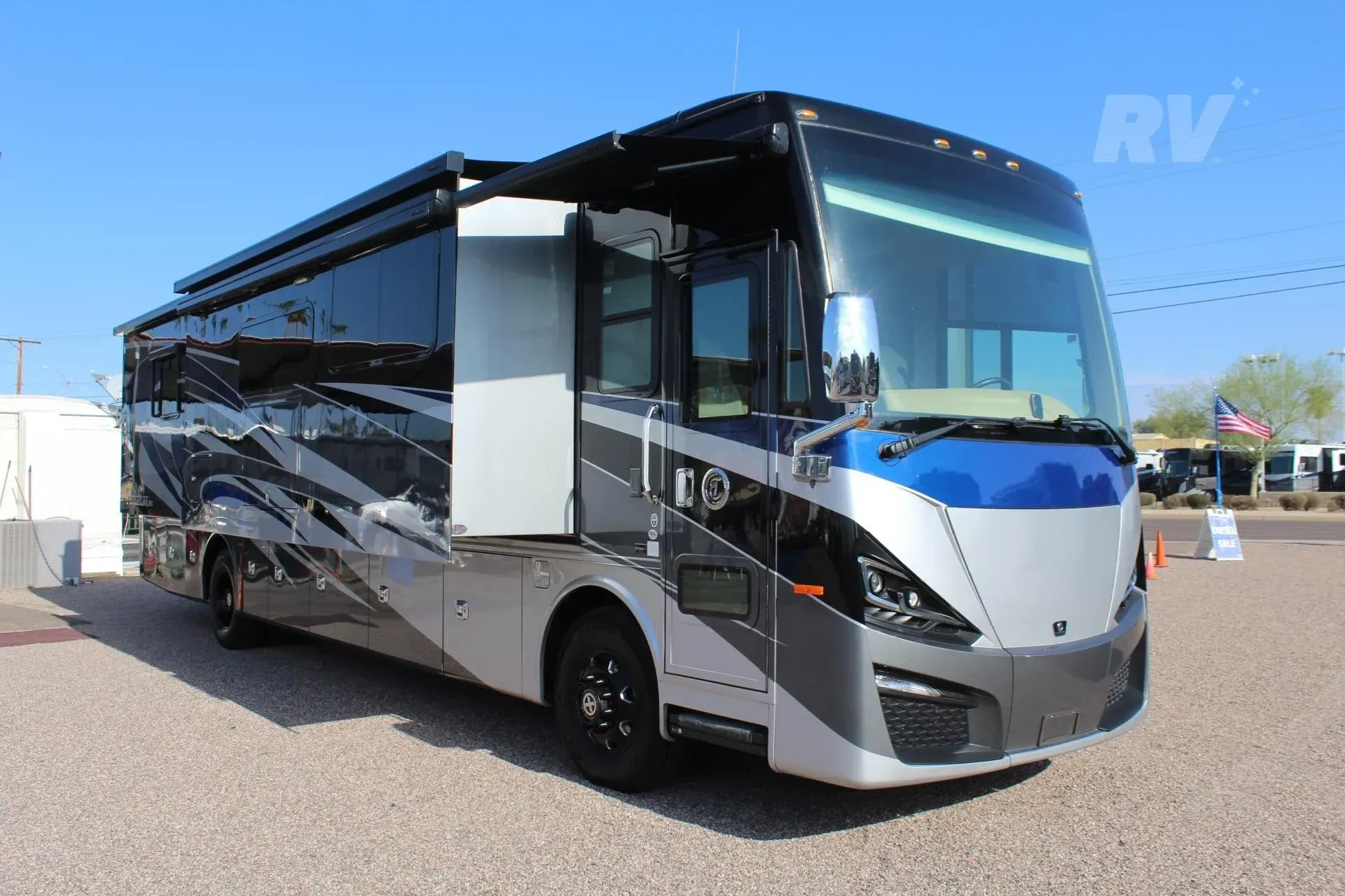 Large, modern RV with blue, silver, and black exterior parked outdoors on a sunny day.