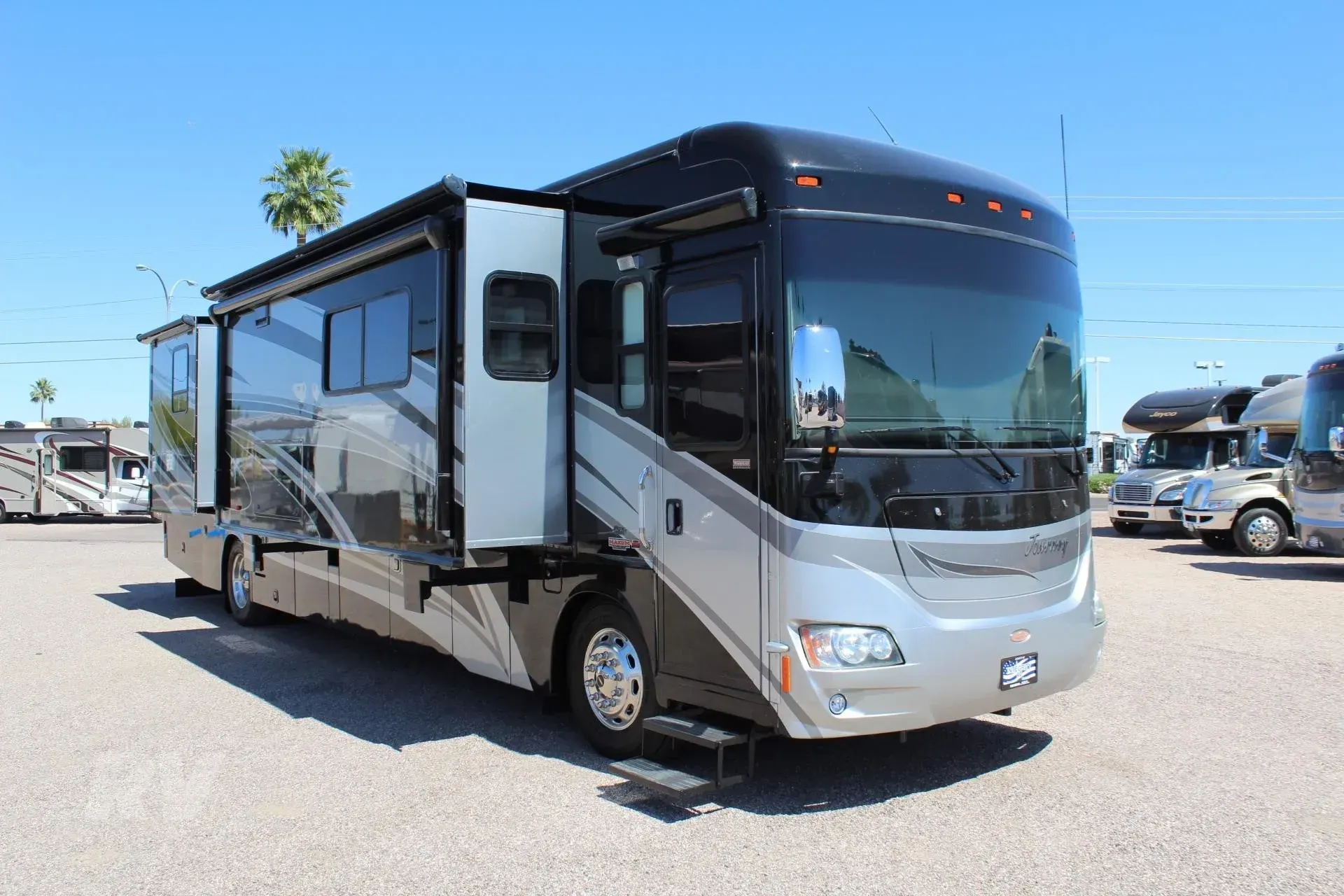 A large, silver and black RV with open slide-outs parked outdoors on a sunny day.