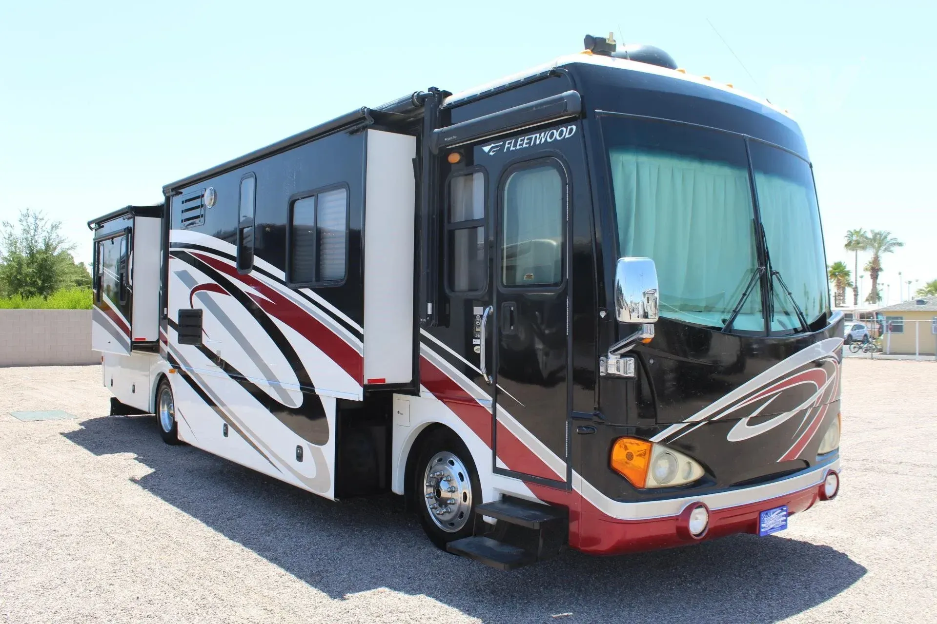 Black and white RV with red accents, parked outdoors with slide-outs extended.