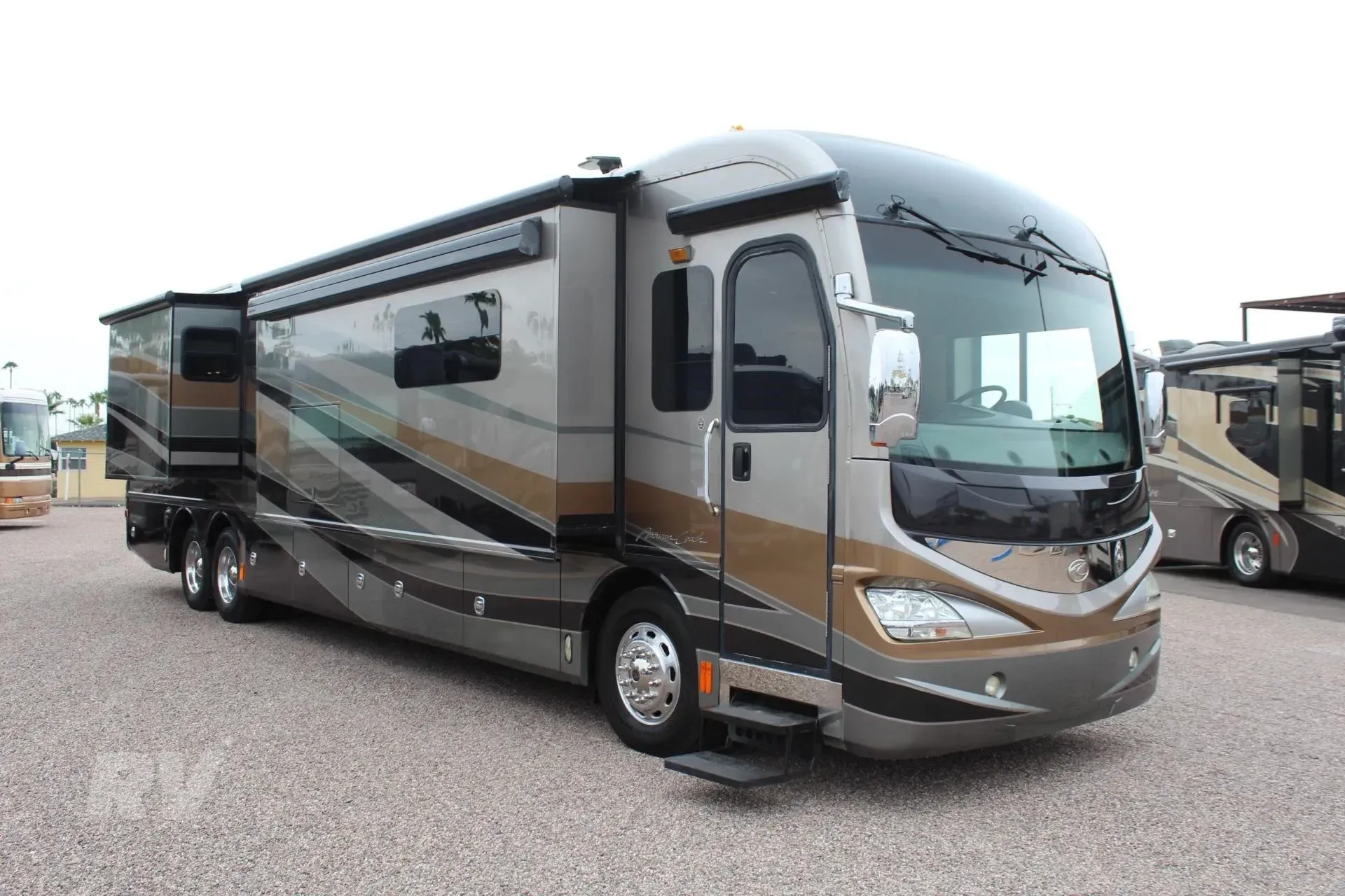 Silver and brown luxury RV parked outdoors on gravel.