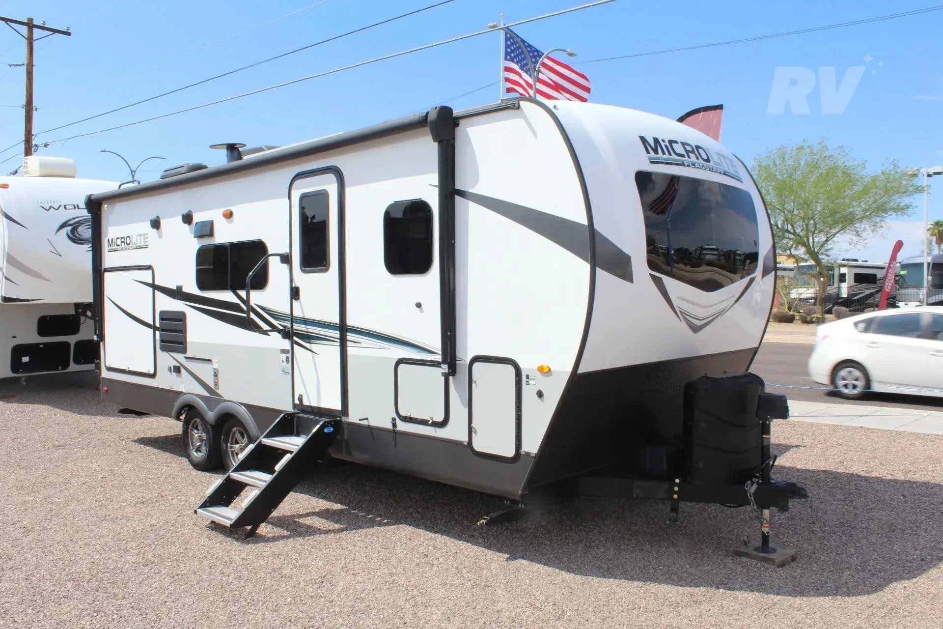 White and gray travel trailer with black accents, parked outdoors, American flag visible.