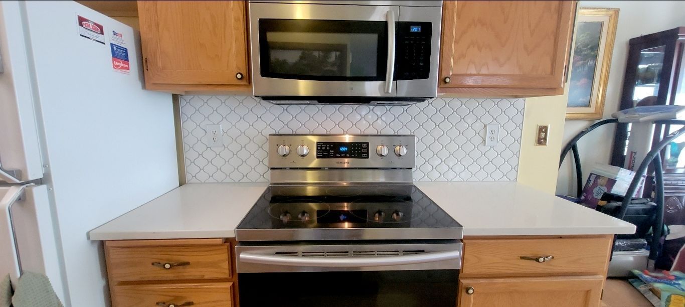 Kitchen with stainless steel appliances: microwave, stove, cabinets, and light countertop. White tile backsplash.