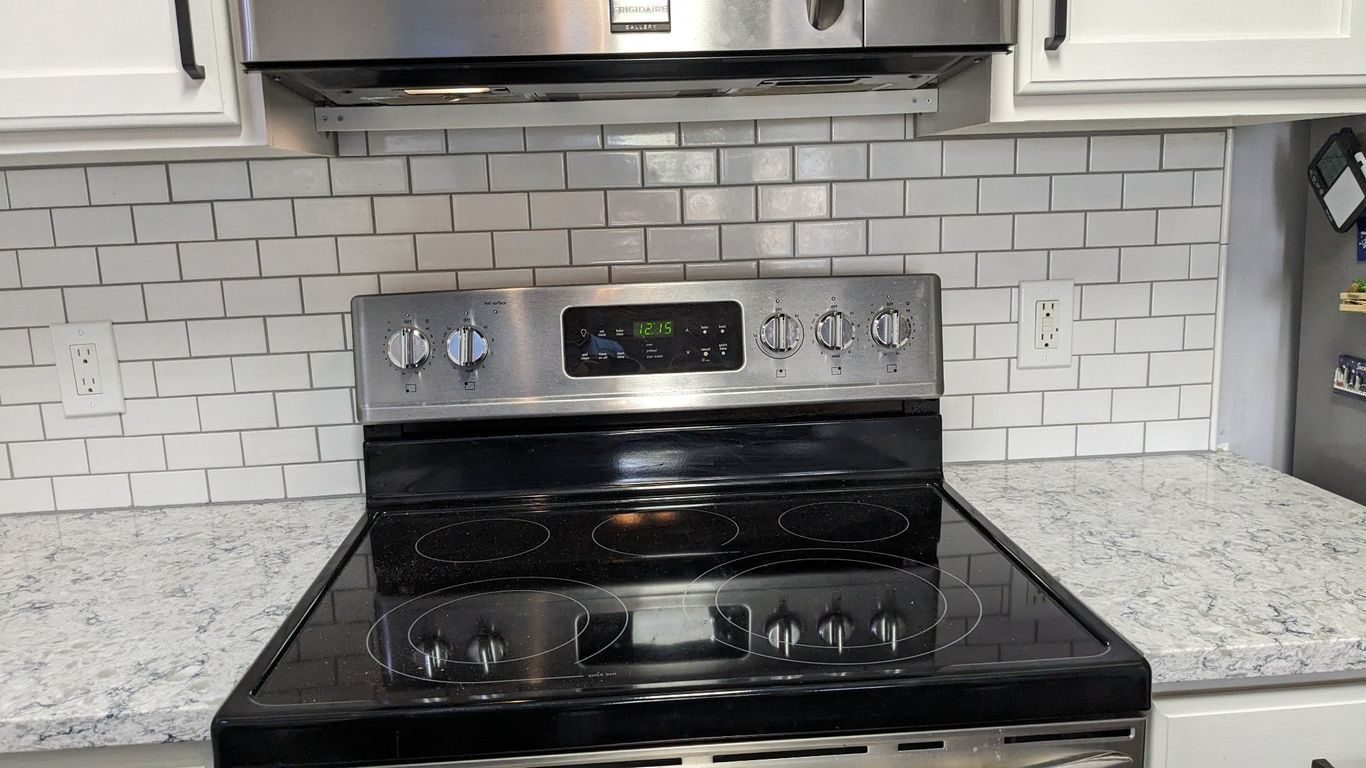 Stainless steel stove under a stainless steel range hood, white subway tile backsplash, light countertops, and white cabinets.
