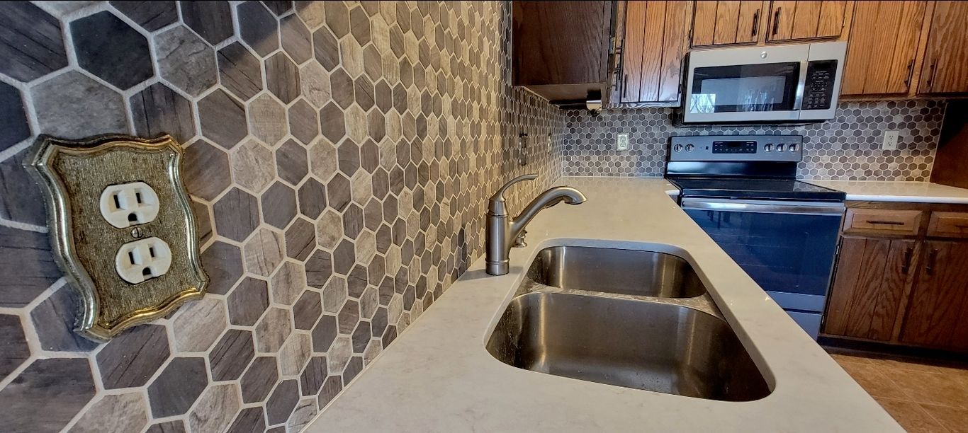 Kitchen with a sink, countertop, and patterned tile backsplash. There is a microwave and stove.