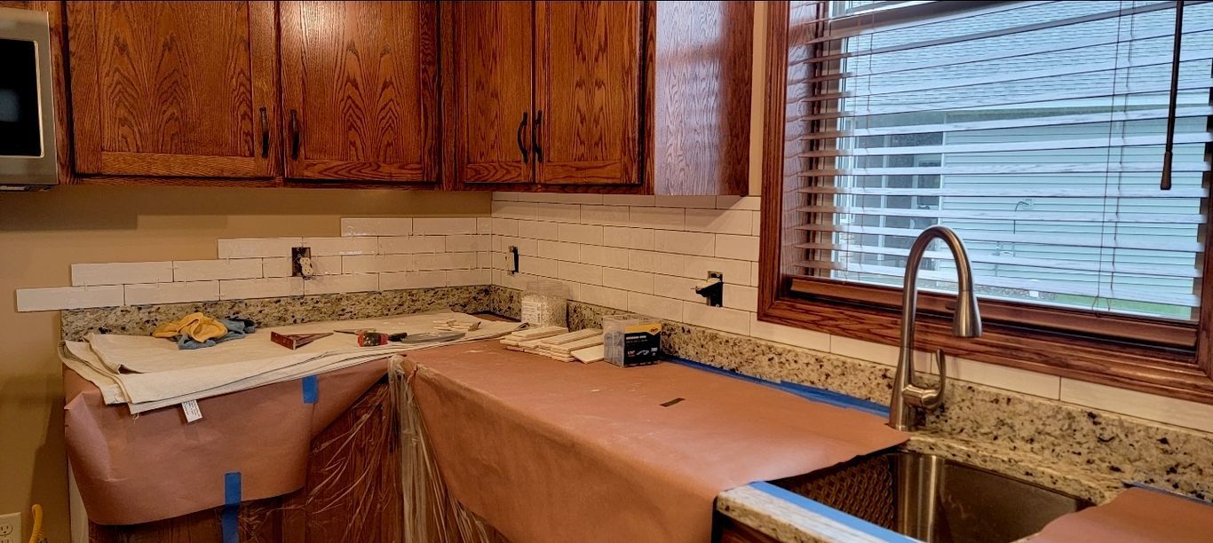 Kitchen with partially tiled backsplash, wood cabinets, granite countertops, and a stainless steel sink.