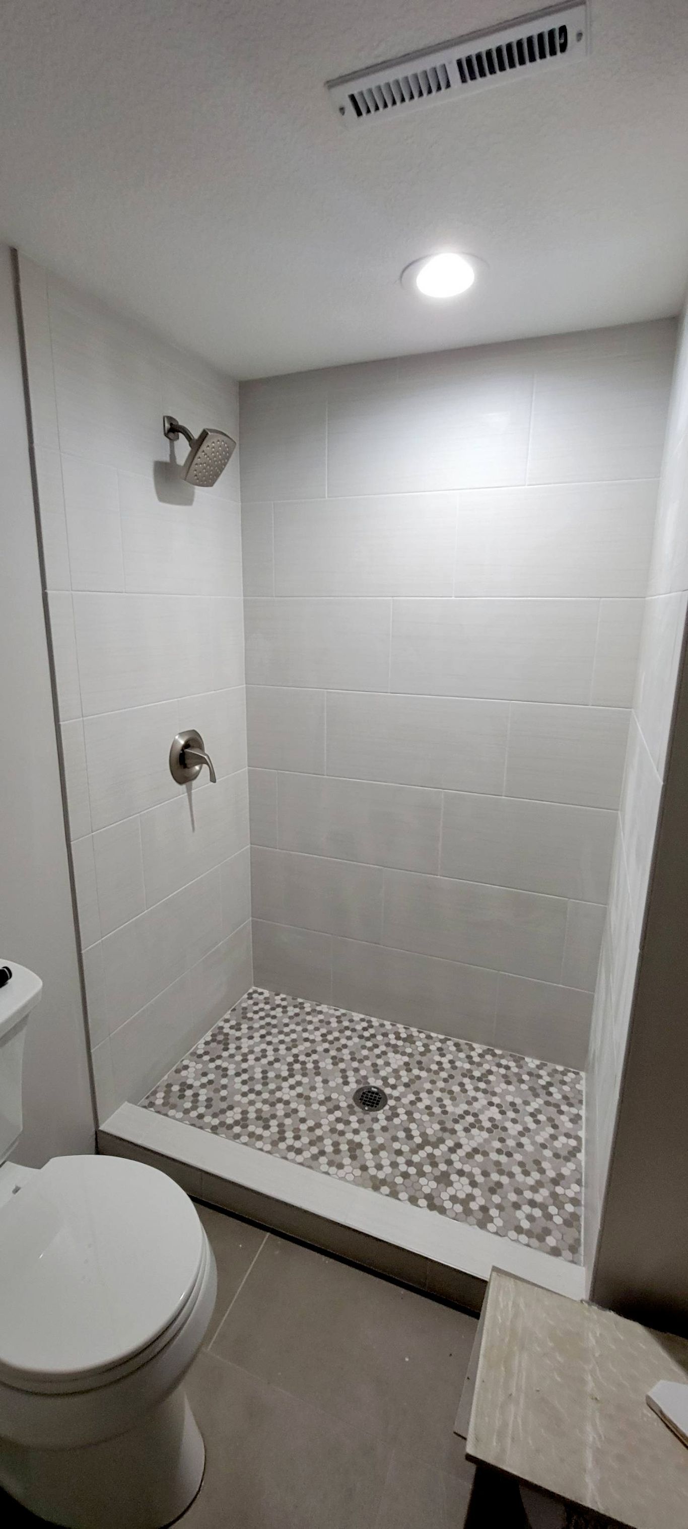 A modern bathroom with a shower stall, a toilet, and pebble flooring. The walls are tiled.