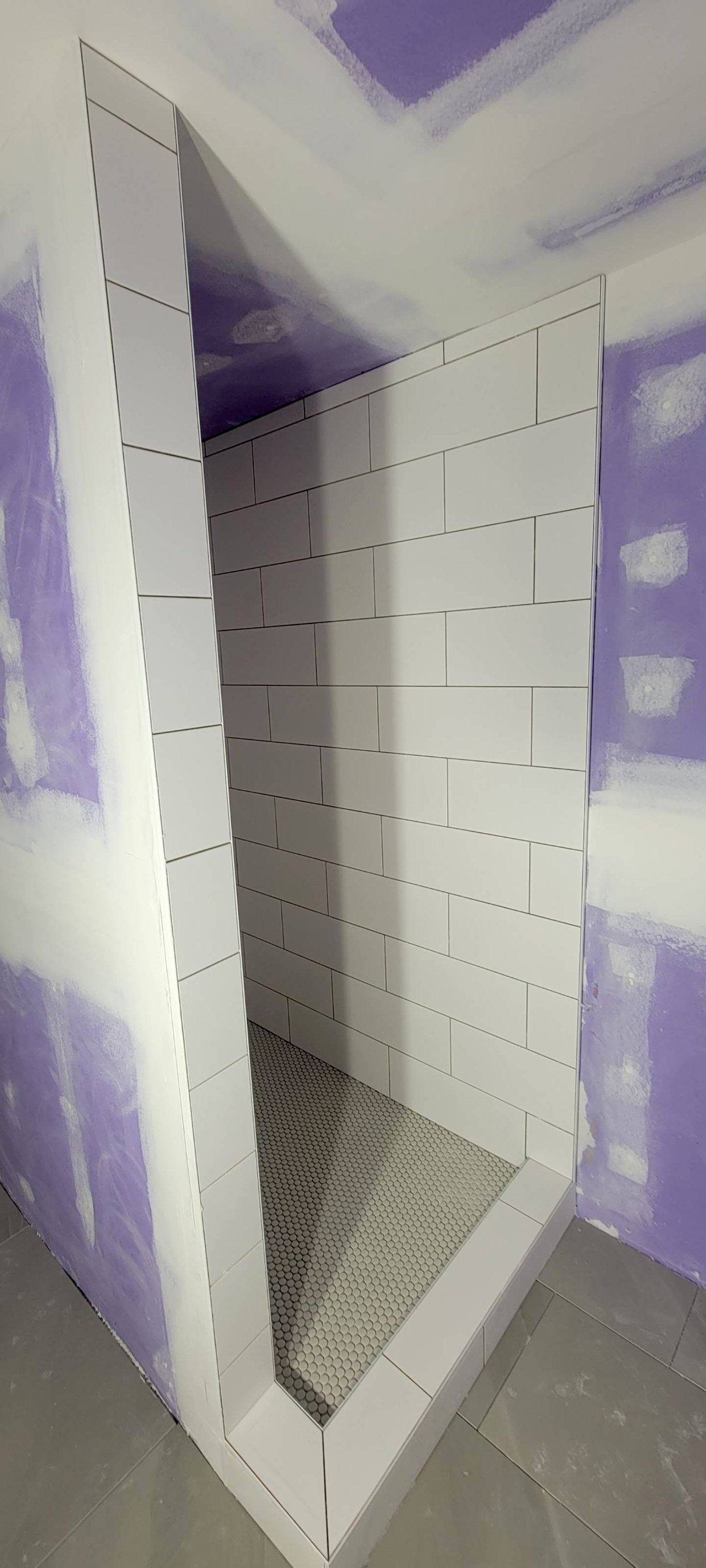 A partially constructed shower stall with white walls and a tiled floor inside a room.