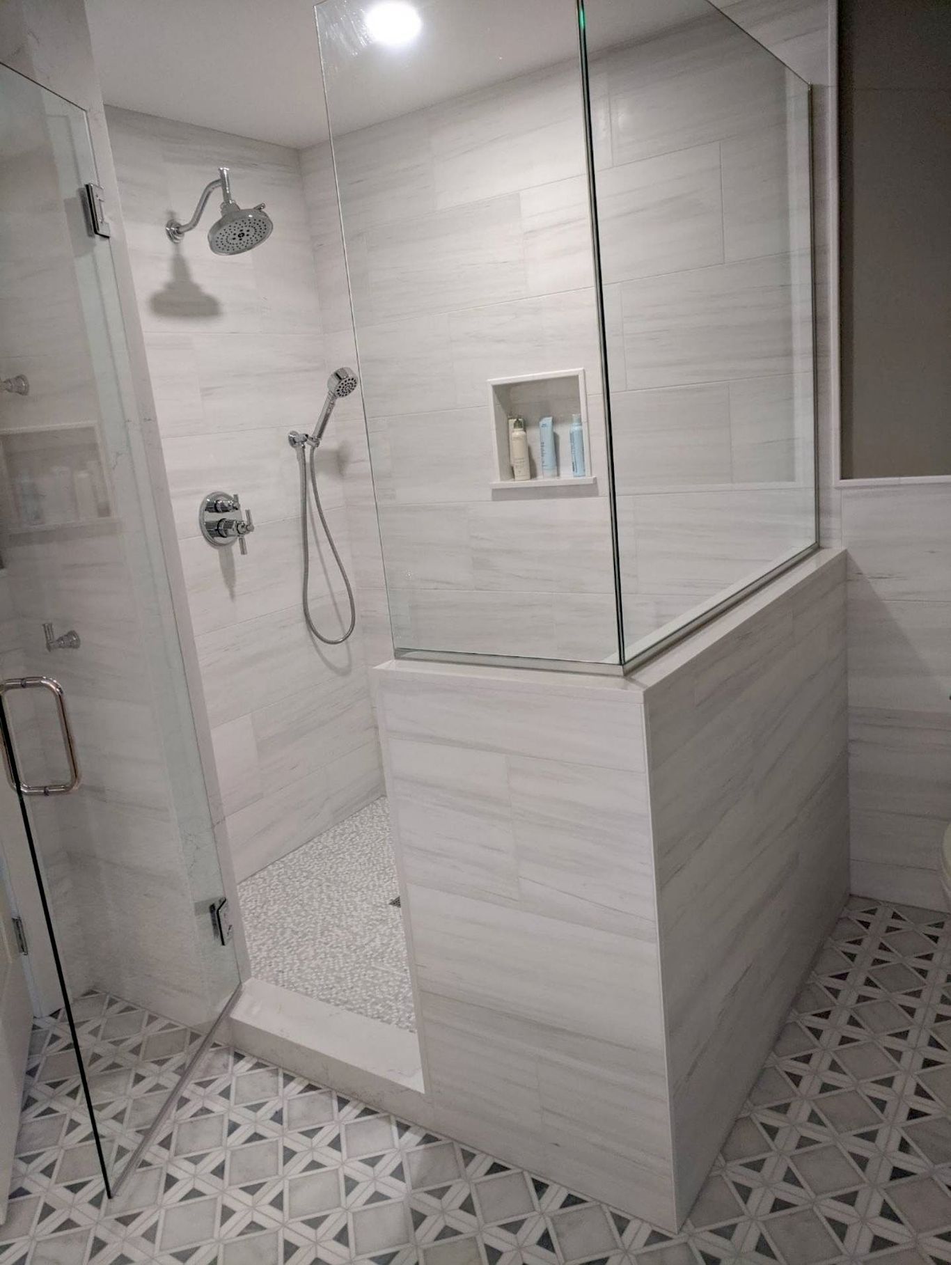 Modern bathroom with glass shower, light gray tiles, and mosaic floor.