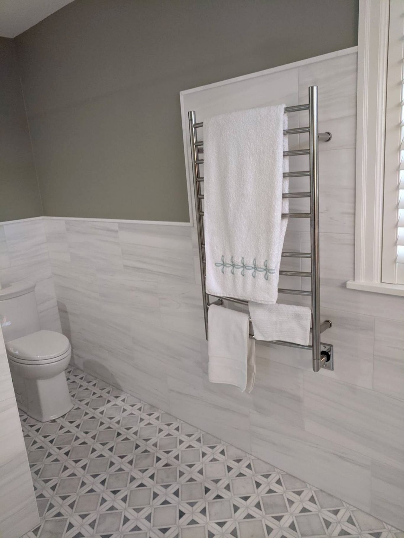 Bathroom with white tiles, a heated towel rack holding white towels, and a toilet.