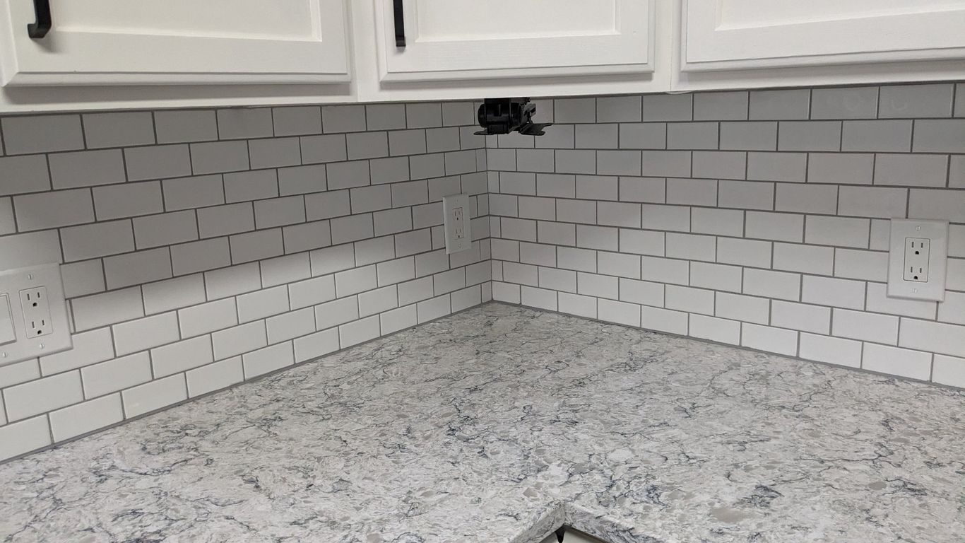 White subway tile backsplash with a speckled gray countertop in a kitchen.