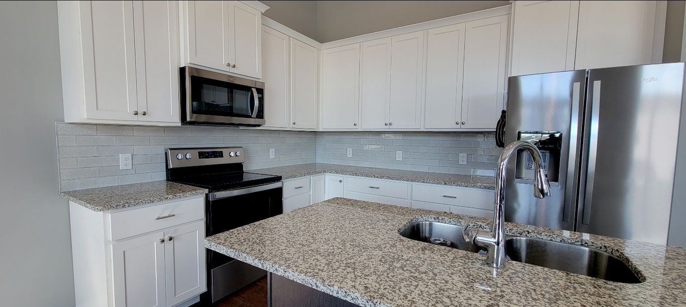 Modern kitchen with white cabinets, granite countertops, and stainless steel appliances.