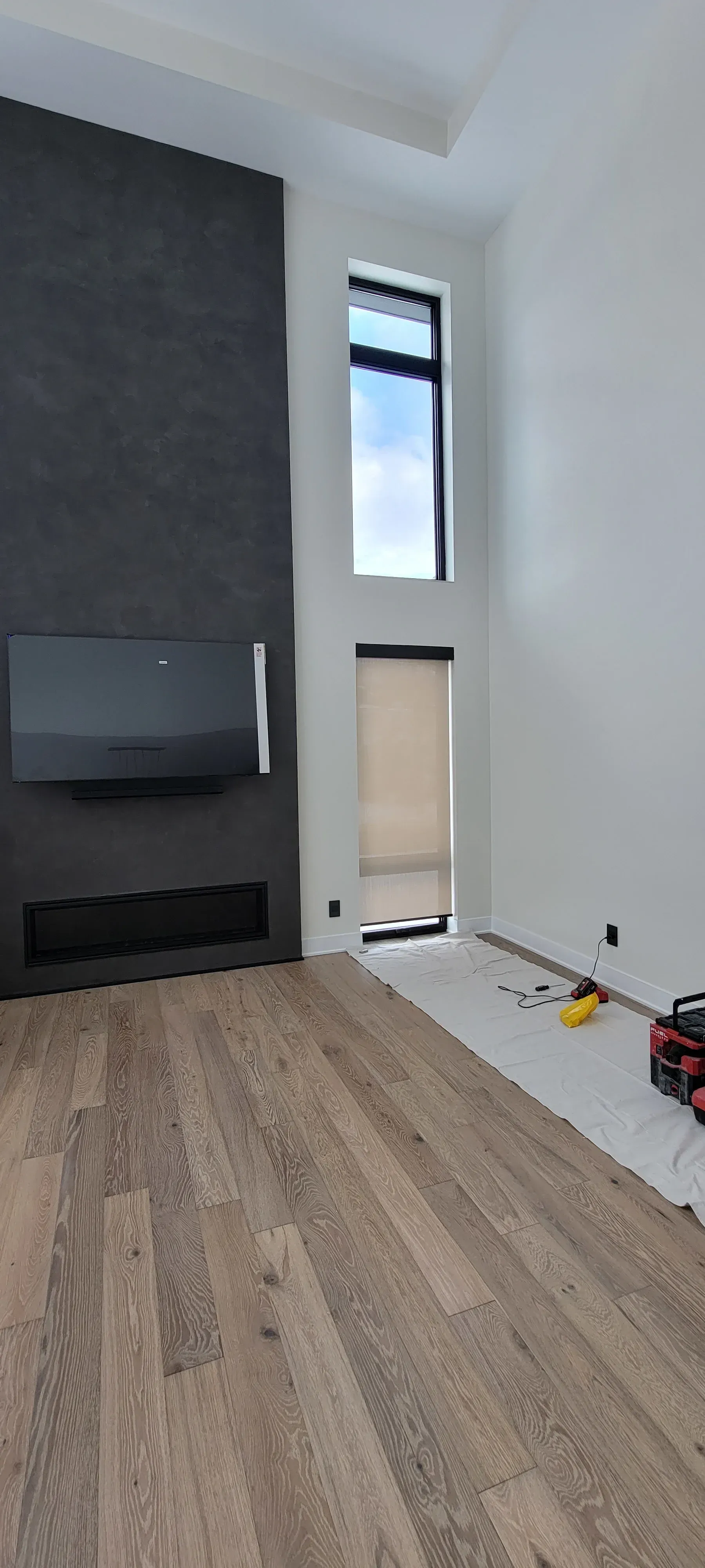 A modern interior with wood flooring, dark accent wall with TV, tall windows, and a fireplace.
