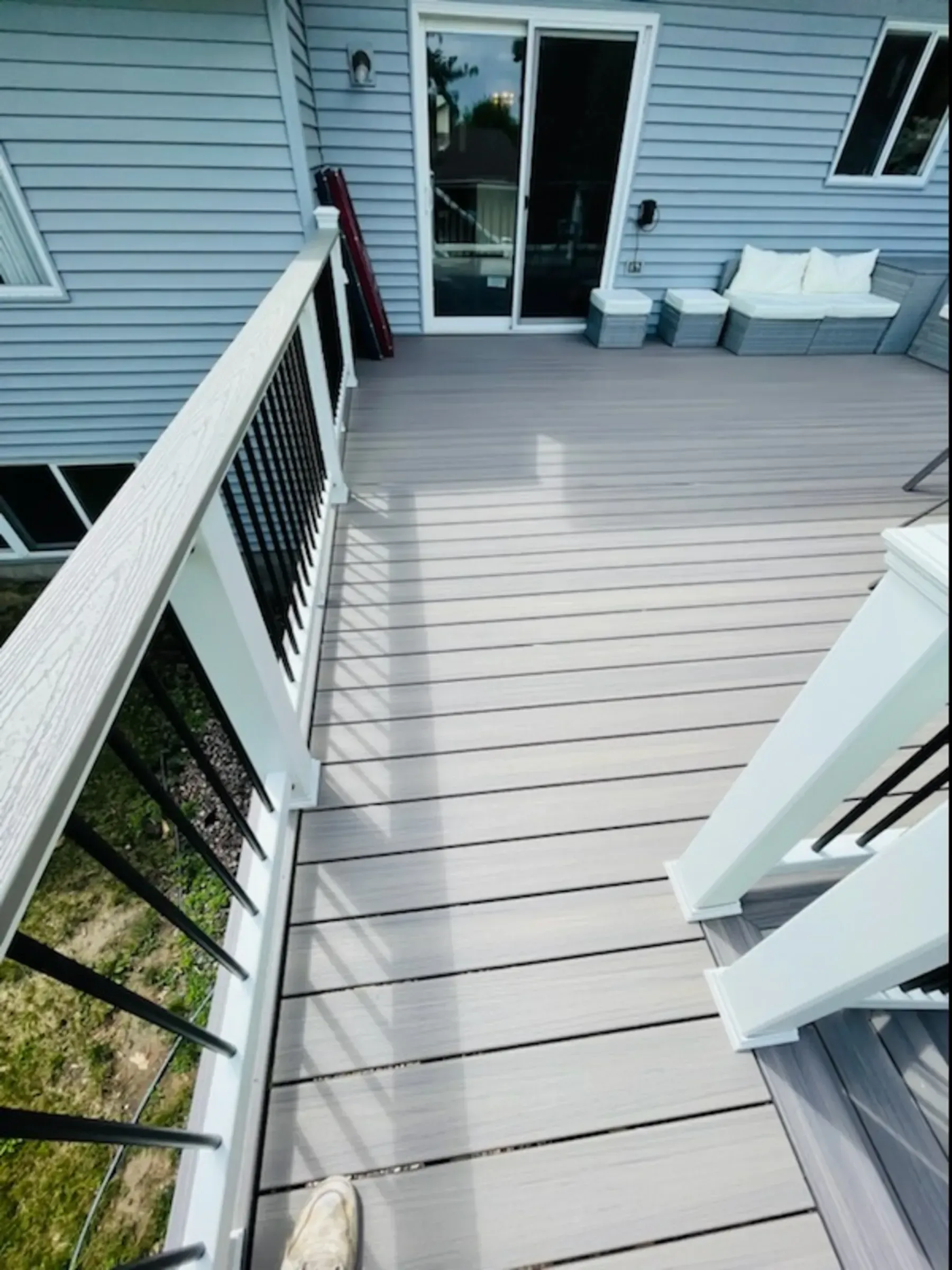 Gray composite deck with white railing and black spindles, leading to a sliding glass door.