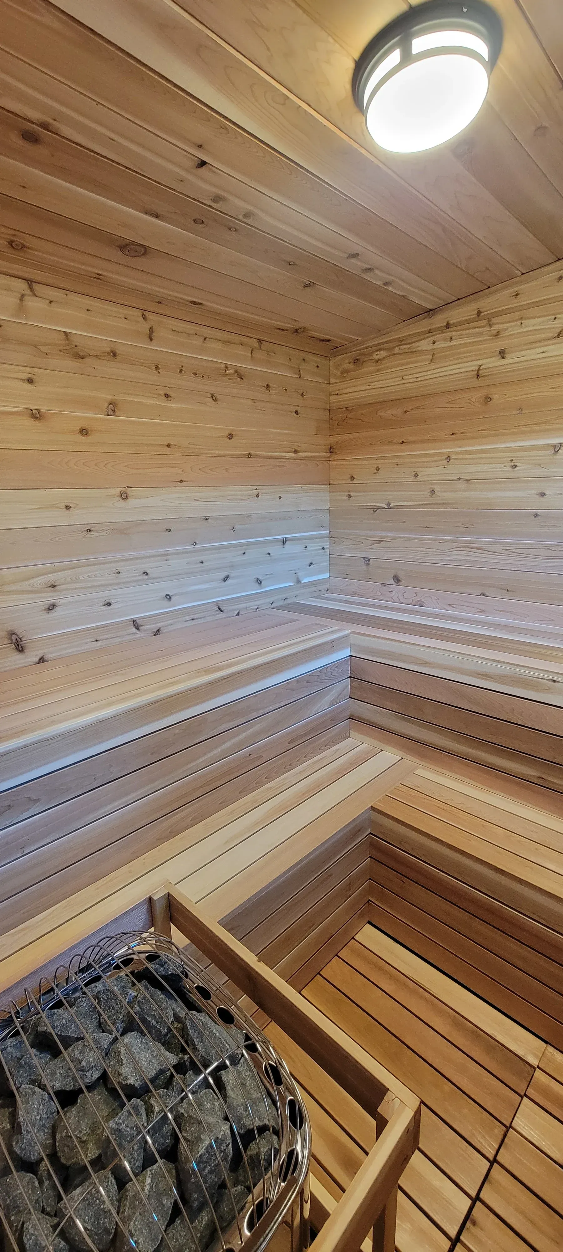 Interior of a wooden sauna with stones. Overhead light is visible.