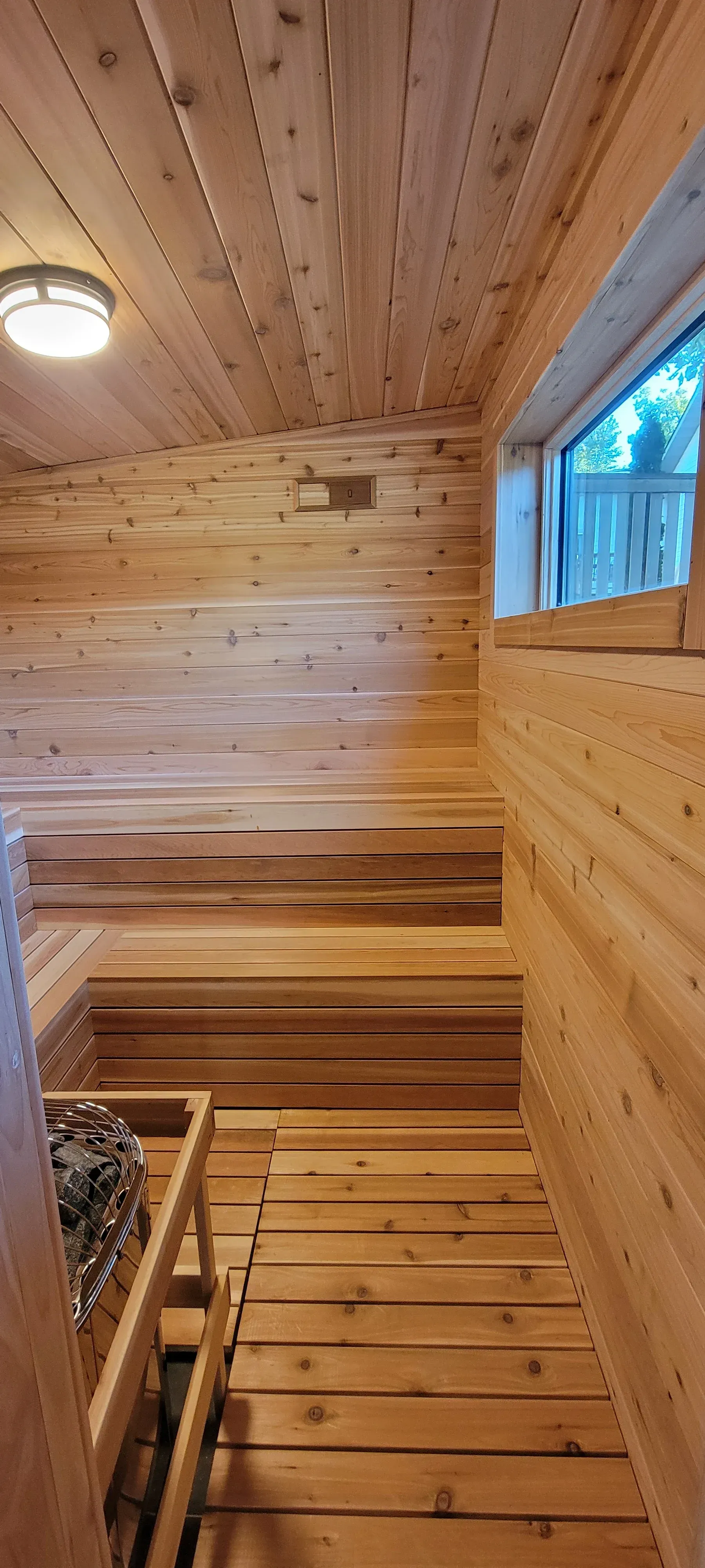 Interior of a wooden sauna with tiered seating, a window, and a heater in the corner.