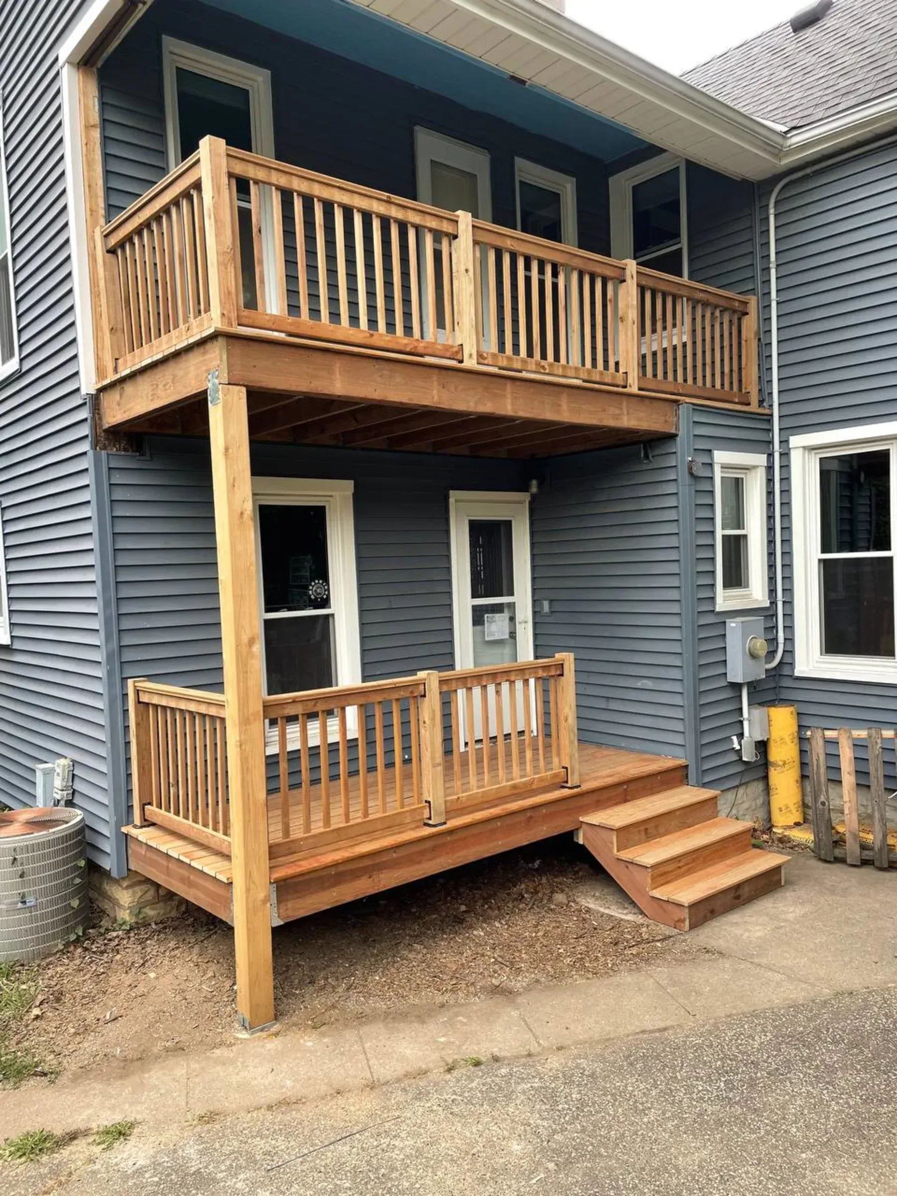 Two-story wooden deck attached to a gray house, with a staircase leading down to the ground level.