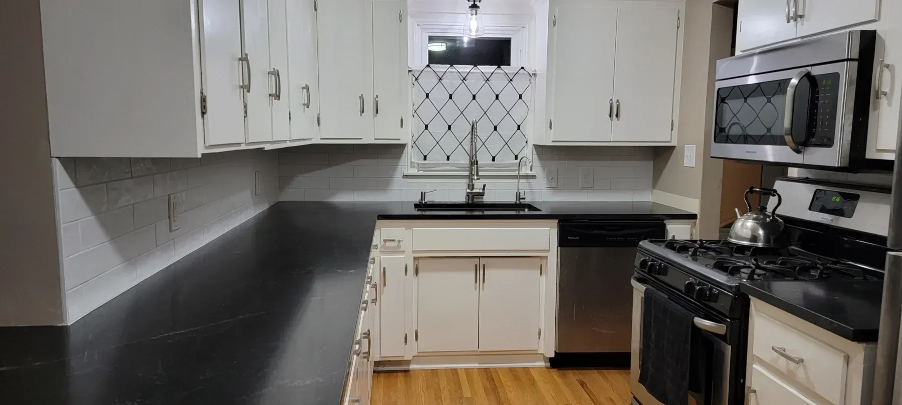 A kitchen with white cabinets, black countertops, and stainless steel appliances.