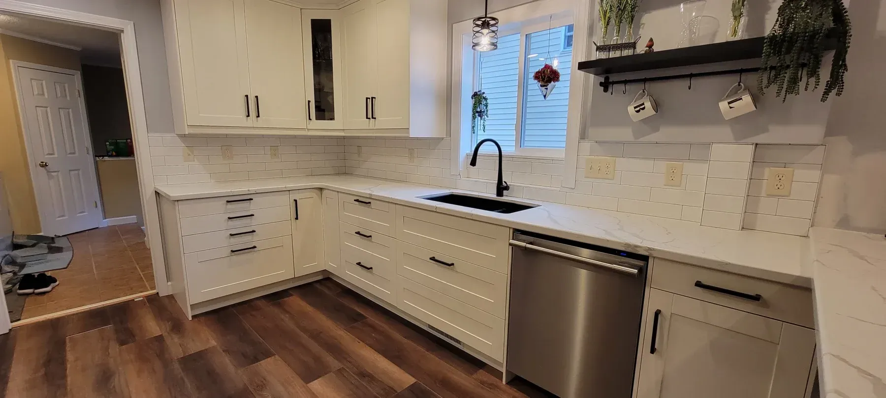 White kitchen with white cabinets, dark hardware, and a black faucet. A stainless-steel dishwasher sits below the counter.