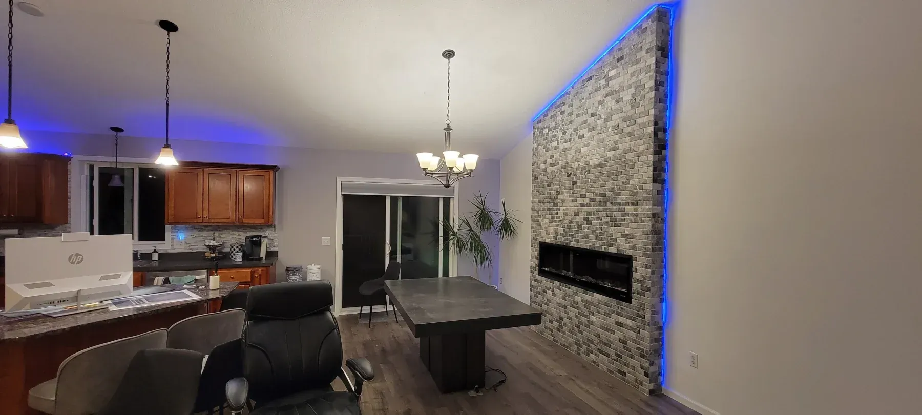 A modern dining area with a stone wall fireplace, a large table, and blue ambient lighting.
