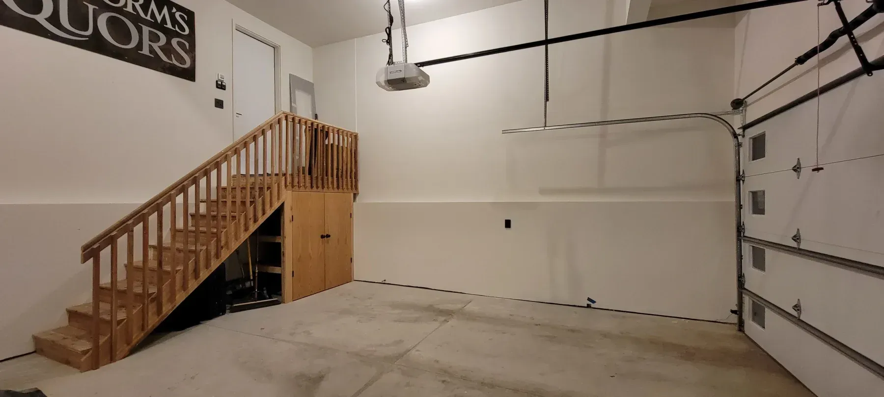 Empty garage interior with stairs, storage, and a garage door.