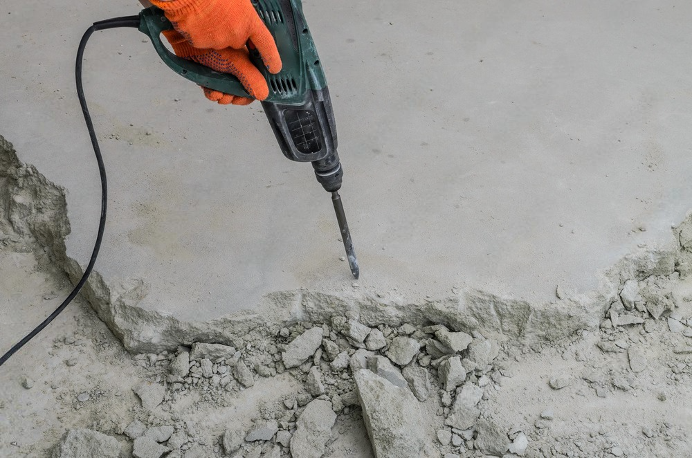 A person is using a hammer drill on a concrete floor.