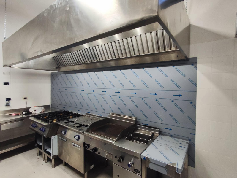 Elettrodomestici da cucina in acciaio inox sotto una grande cappa. 