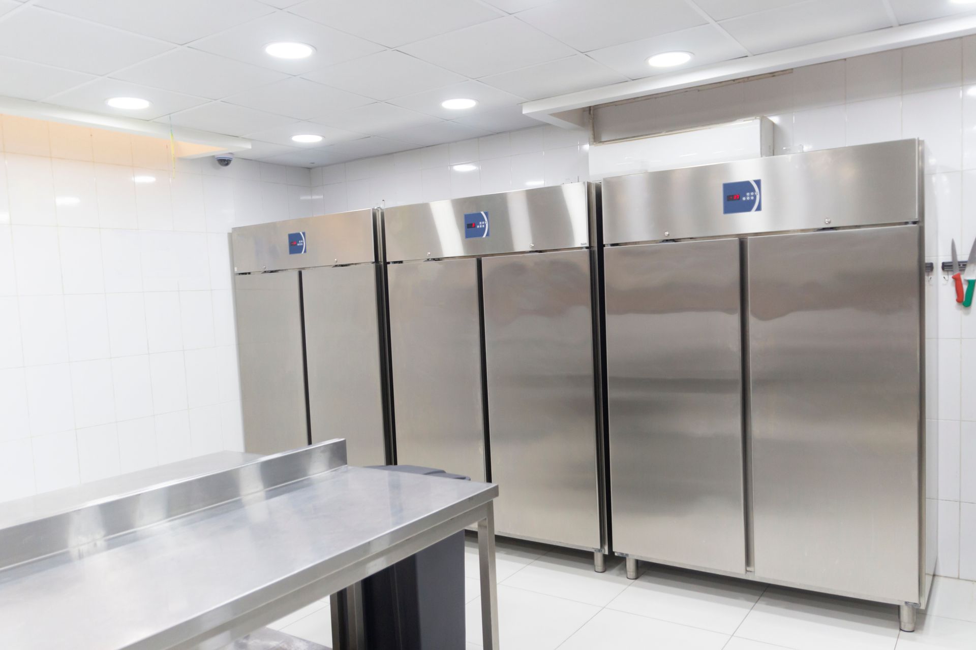 Cucina commerciale con frigoriferi in acciaio inox e tavolo di preparazione in metallo.