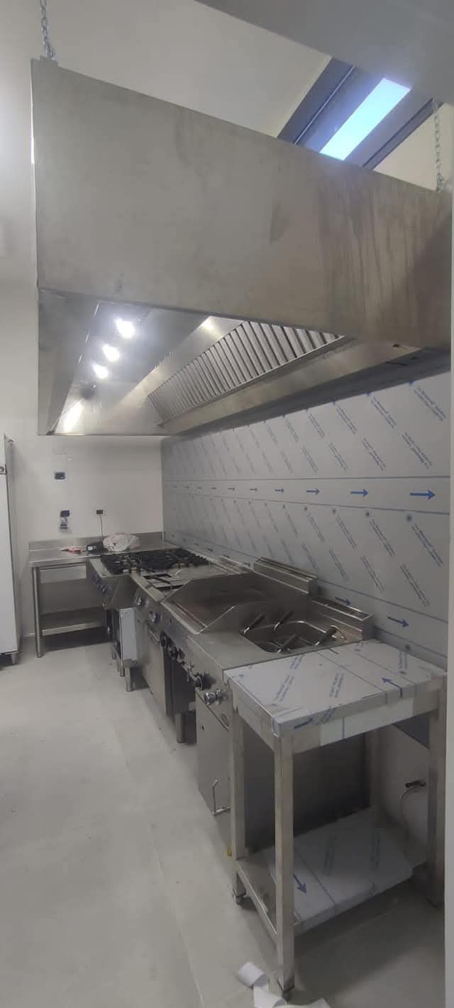 Una cucina commerciale in acciaio inossidabile con una grande cappa e attrezzature per cucinare.