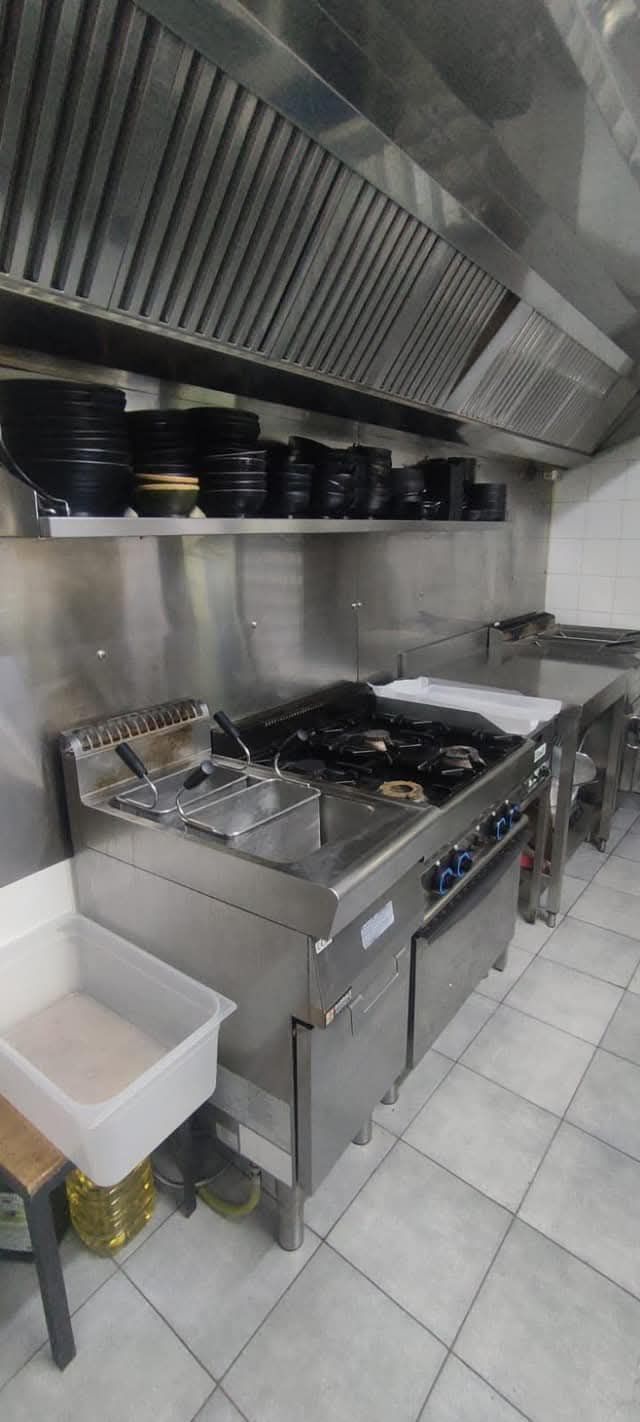 Una cucina commerciale in acciaio inossidabile con fornelli, cappa aspirante e ripiani con piatti neri.