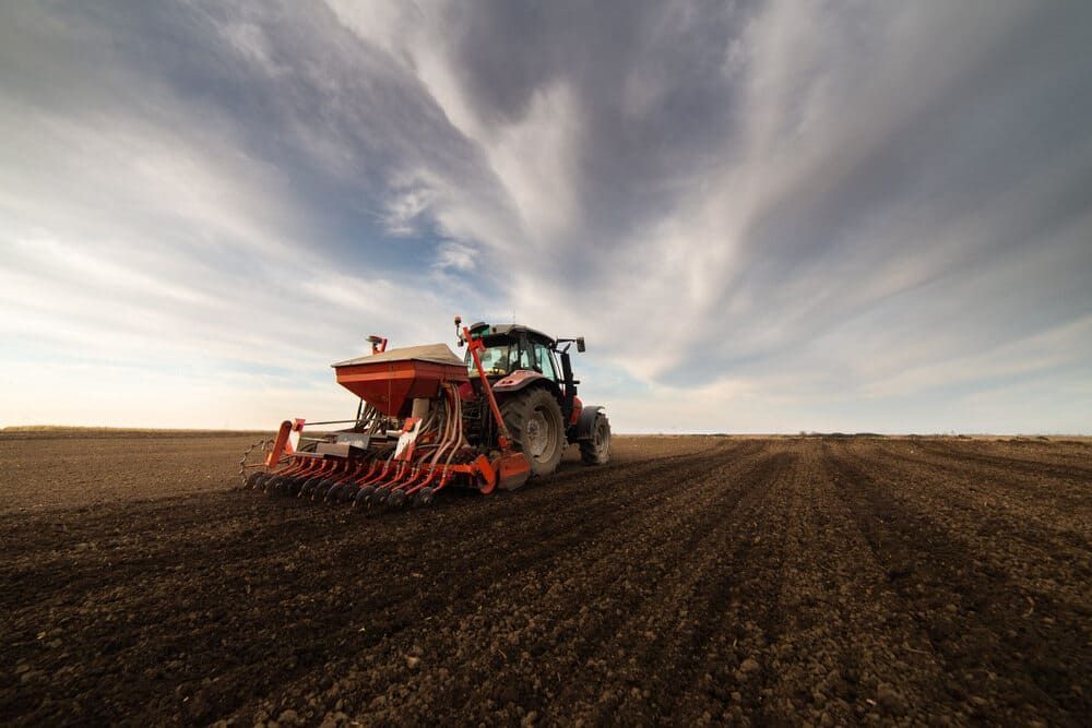 A Tractor Is Plowing A Field On A Cloudy Day — Leslie Farm & Garden Machinery In South Grafton, NSW