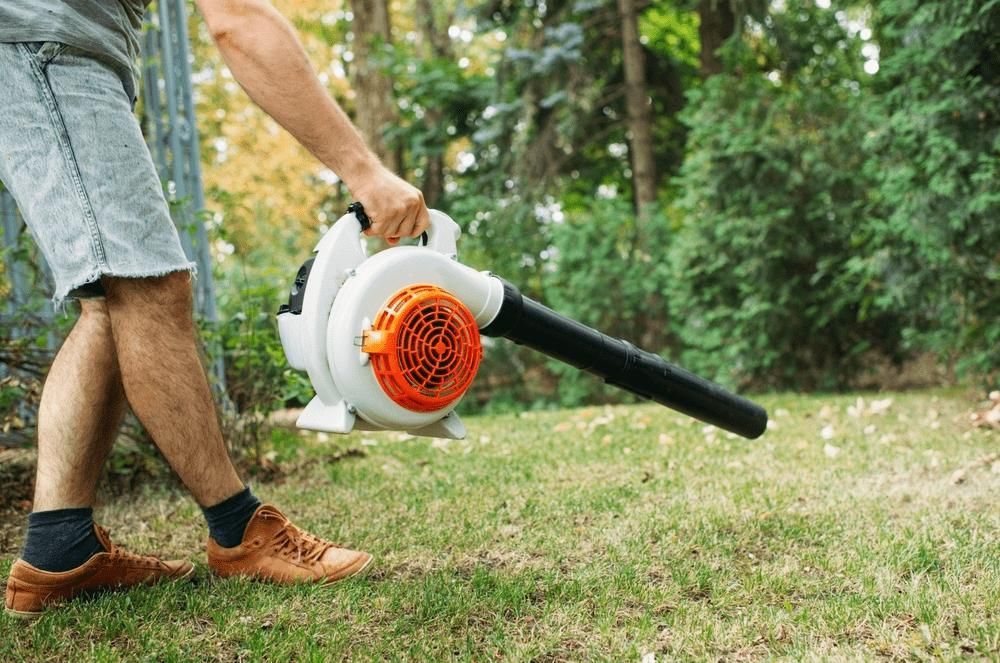 A Man Is Blowing Leaves In A Yard With A Blower — Leslie Farm & Garden Machinery In South Grafton, NSW
