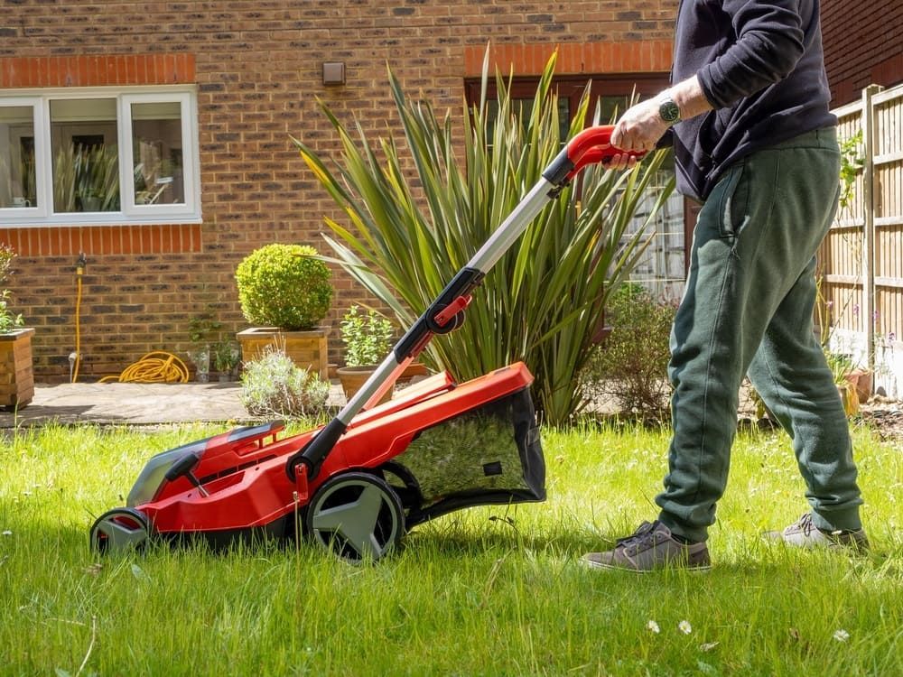 A Man Is Mowing His Lawn With A Red Lawn Mower — Leslie Farm & Garden Machinery In South Grafton, NSW