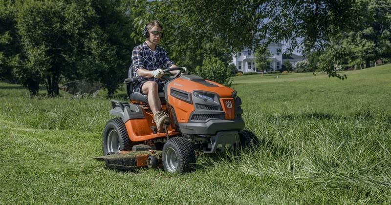 Man riding a ride-on lawn mower across a grassy lawn on a sunny day.