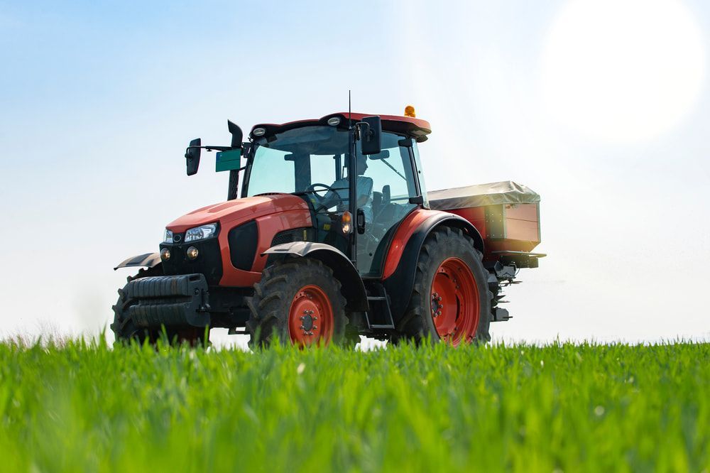 Orange Tractor With a Fertilizer Spreader Driving — Leslie Farm & Garden Machinery In South Grafton, NSW
