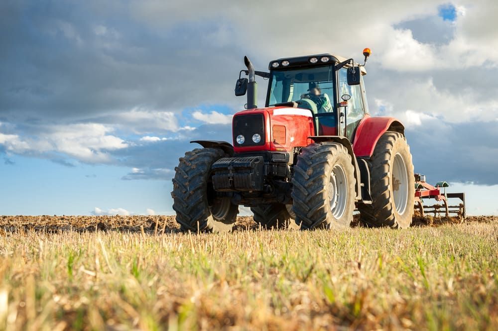 A Red Tractor Is Plowing A Field On A Cloudy Day — Leslie Farm & Garden Machinery In South Grafton, NSW