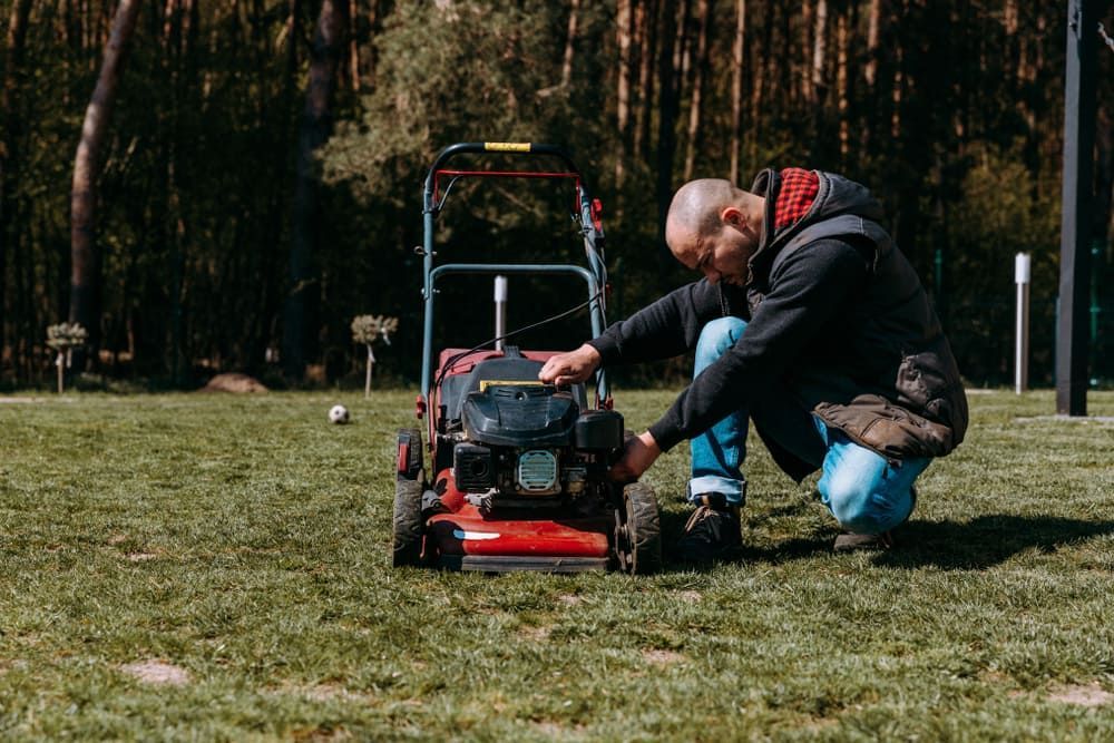 A Man Is Kneeling Down In Front Of A Lawn Mower — Leslie Farm & Garden Machinery In South Grafton, NSW