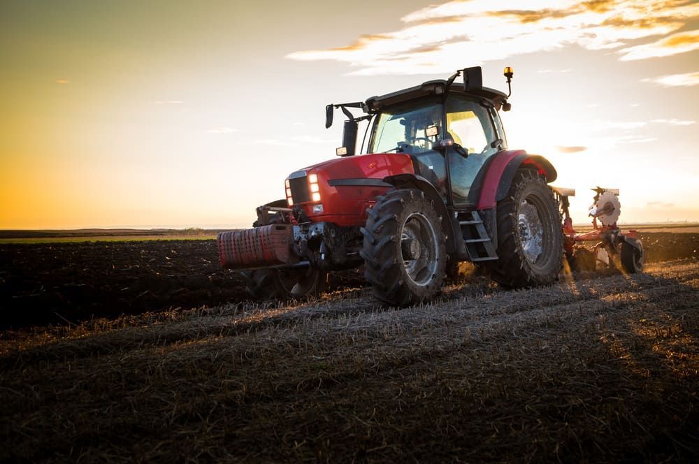 A Red Tractor Is Plowing A Field At Sunset — Leslie Farm & Garden Machinery In South Grafton, NSW