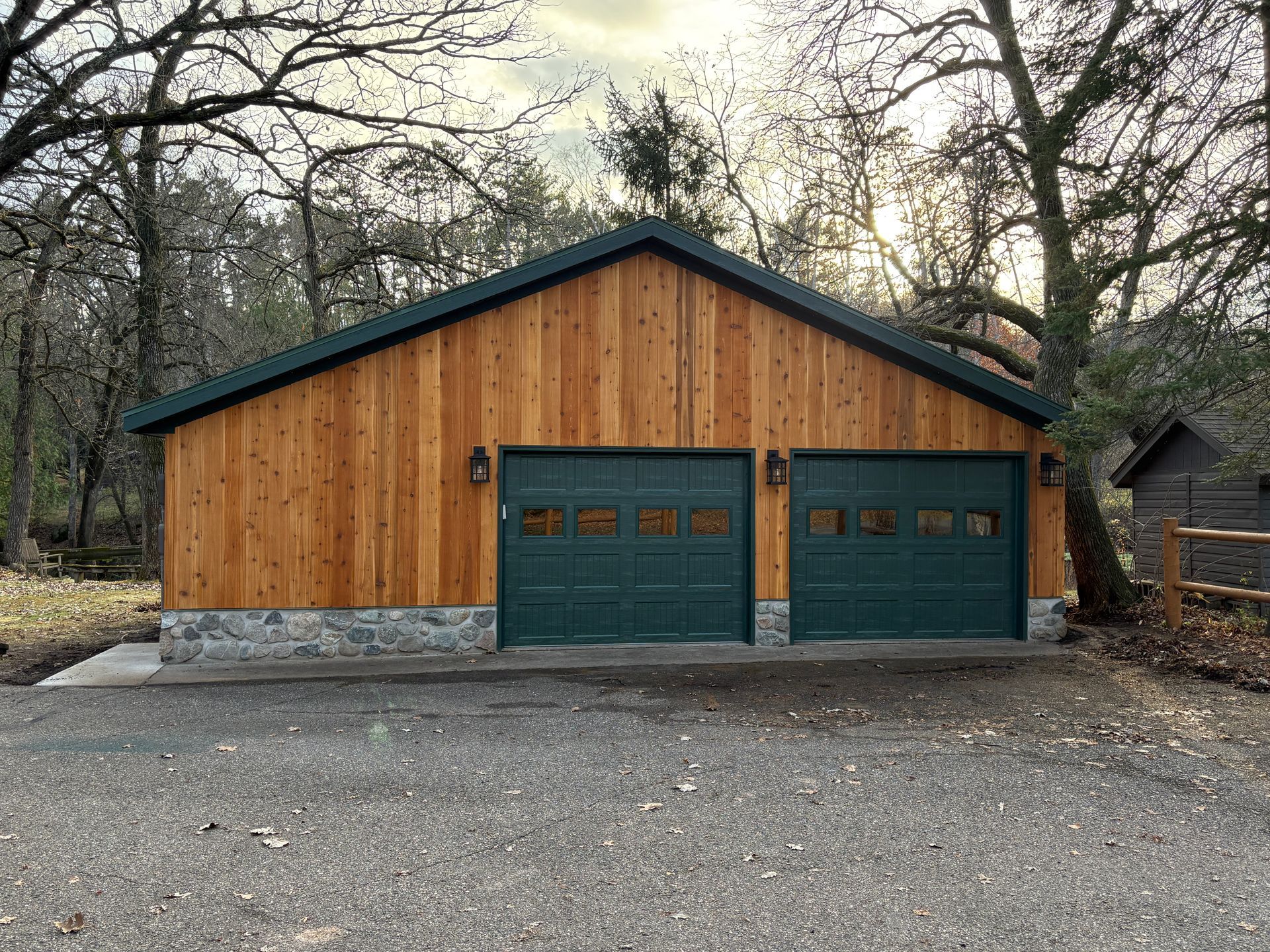 A garage with a wooden siding and green garage doors.
