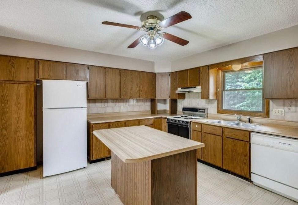 A kitchen with wooden cabinets, a central island, a white refrigerator, a white dishwasher, and a ceiling fan.