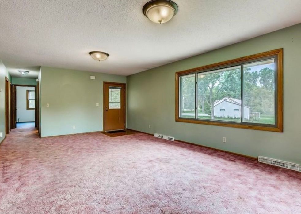 An empty living room with a red carpet and two windows.