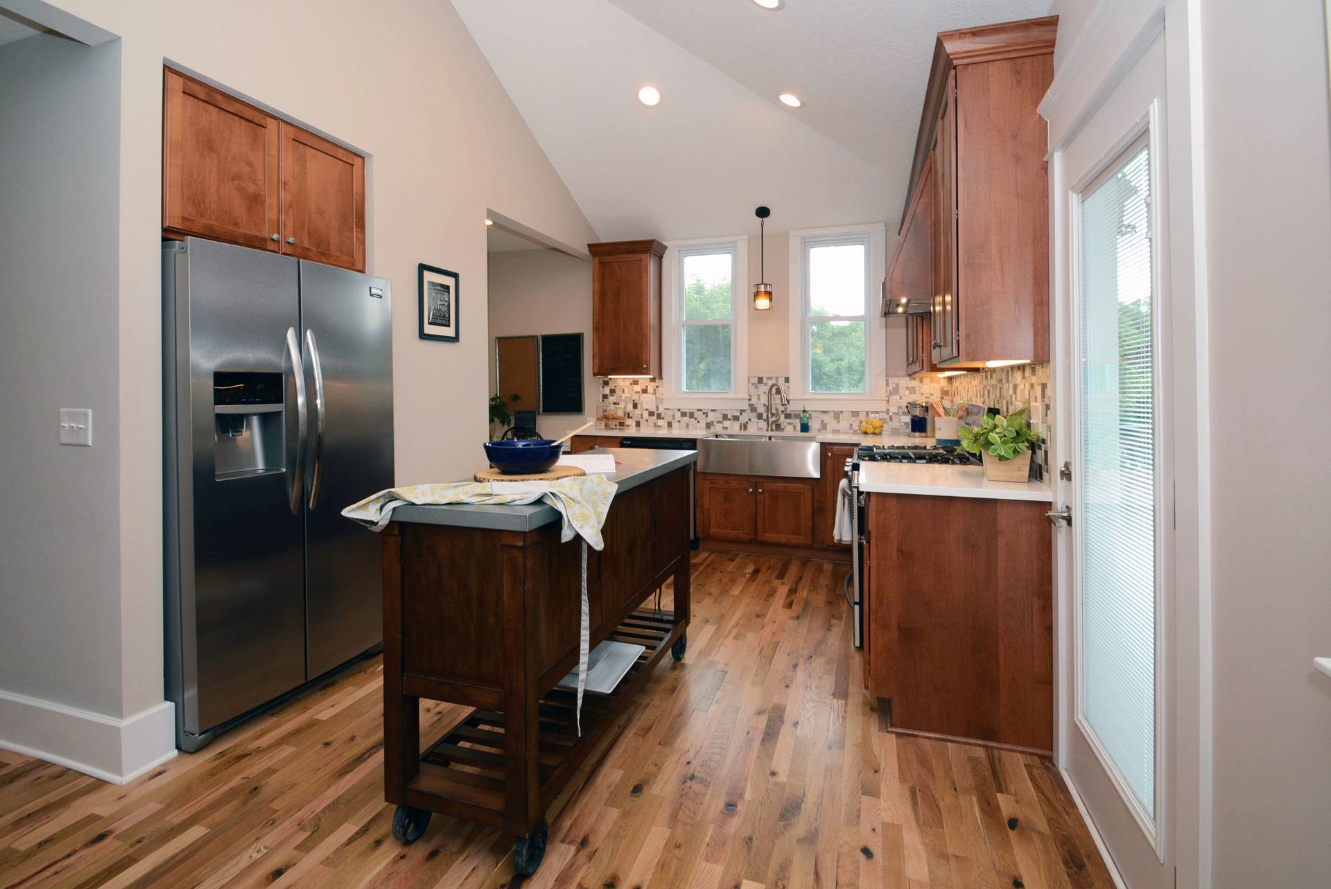 A modern kitchen features wood cabinets, stainless steel appliances, an island on wheels, and hardwood floors.