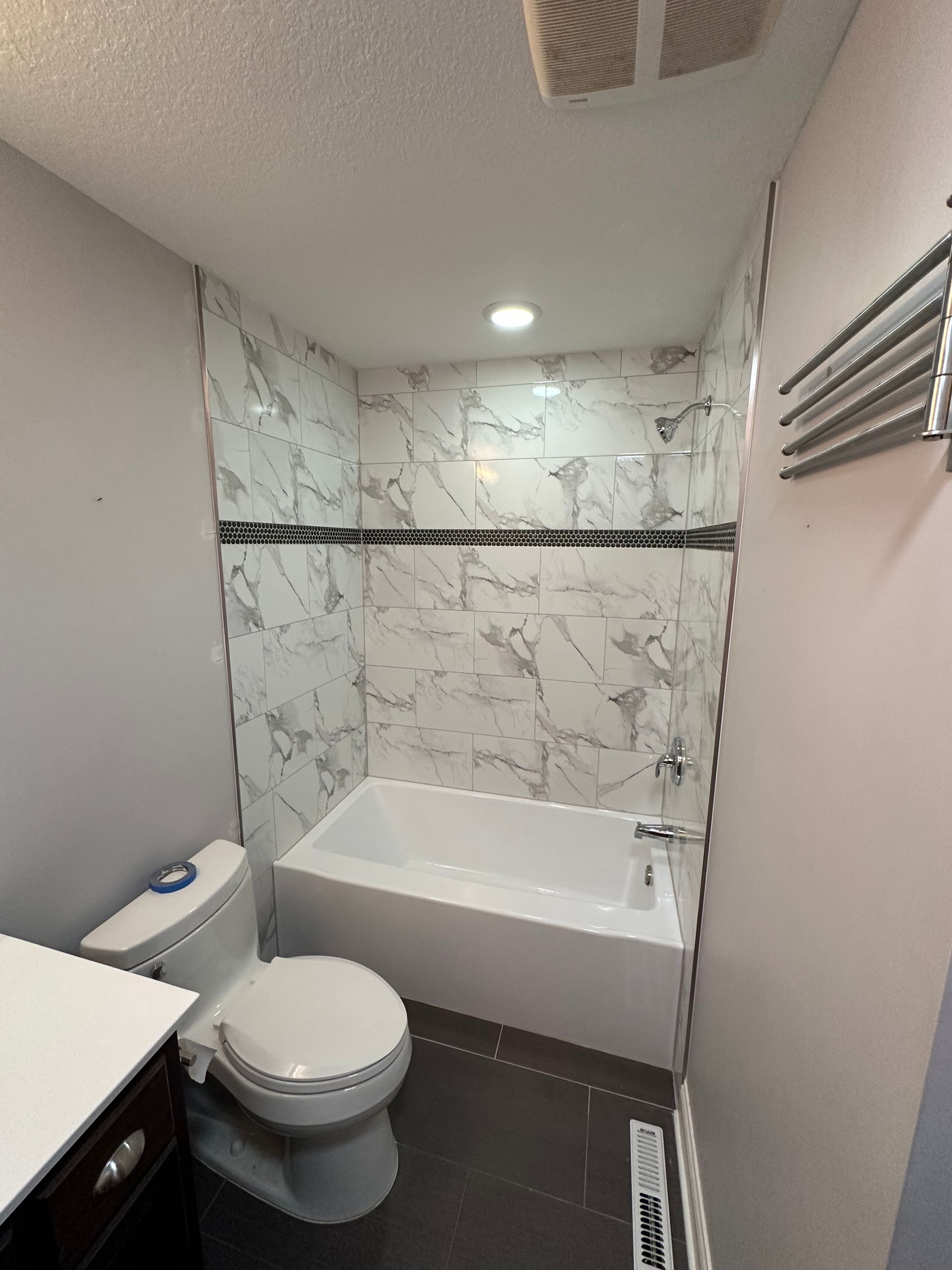 Small bathroom with white and gray tiled shower over a bathtub, with a toilet and sink.