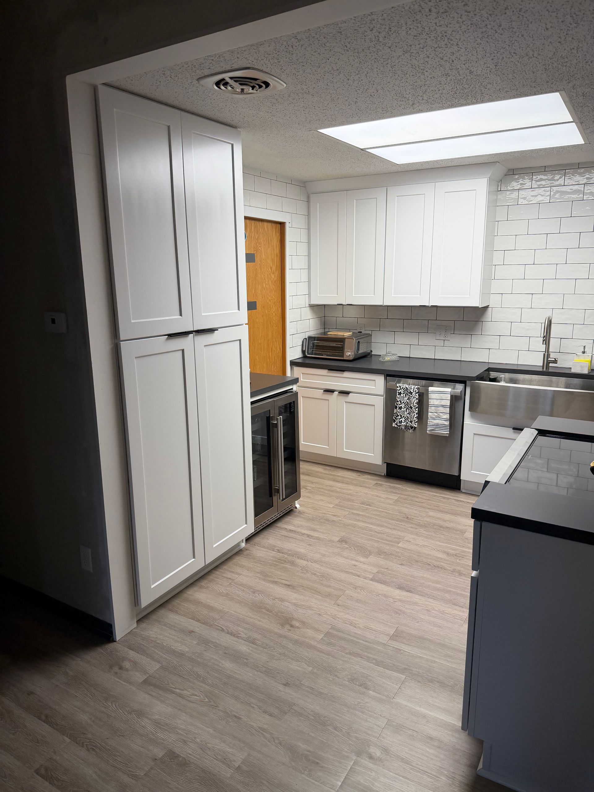 White kitchen with cabinets, stainless steel appliances, and wood-look flooring. A skylight provides natural light.