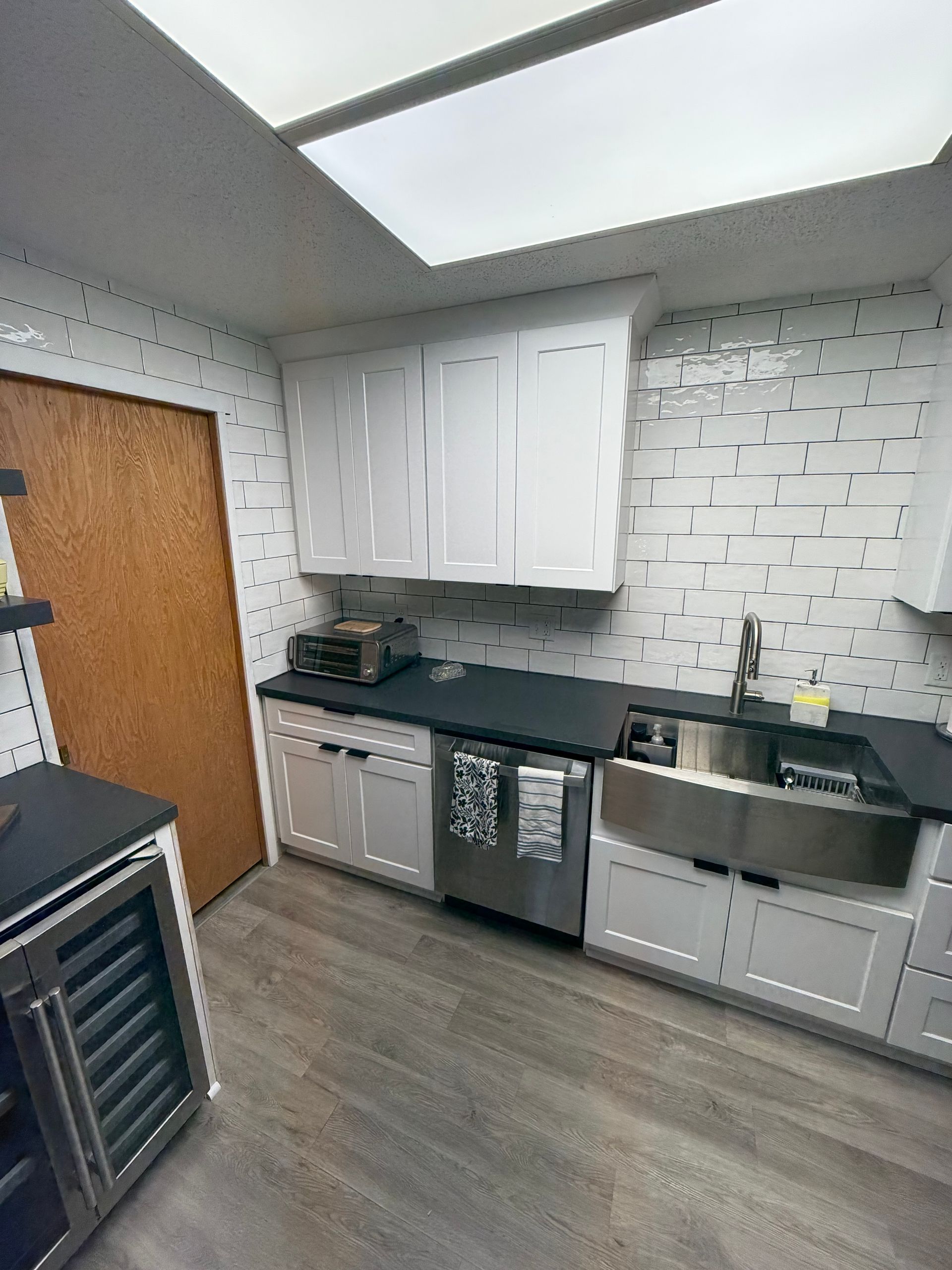 White kitchen with black countertops, stainless steel sink, and wood-look flooring.