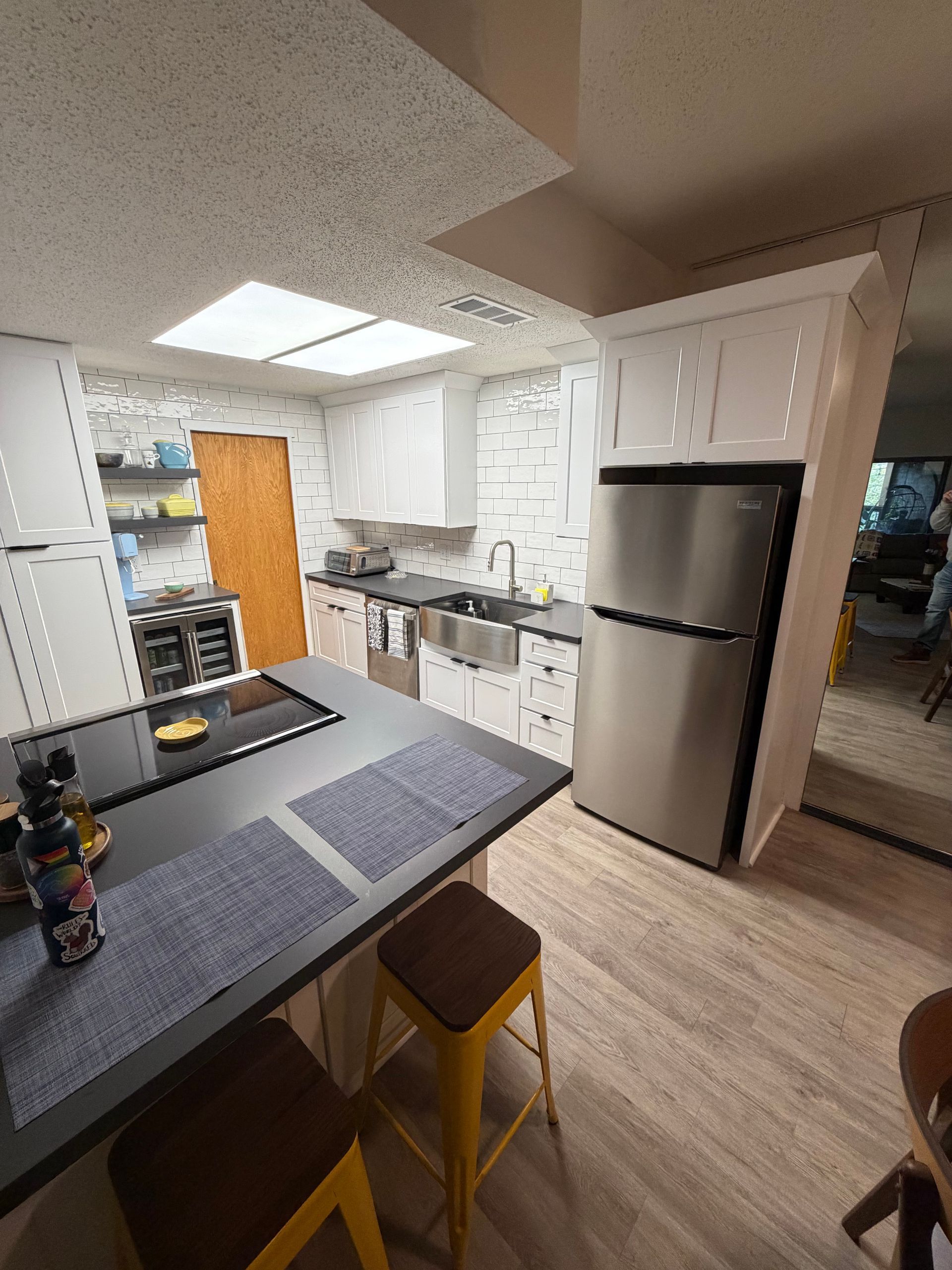 Modern kitchen with island, stainless steel refrigerator, white cabinets, and yellow stools.