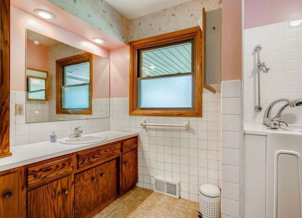 Bathroom with wooden vanity, white tile, window, and pink walls.