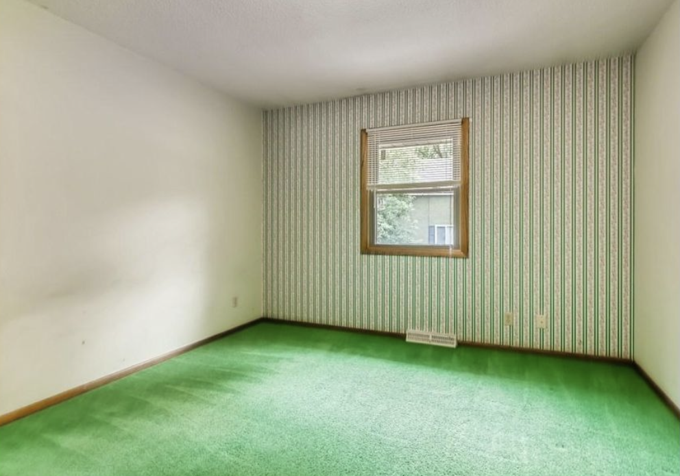 Empty room with green carpet, striped wallpaper, and a window.