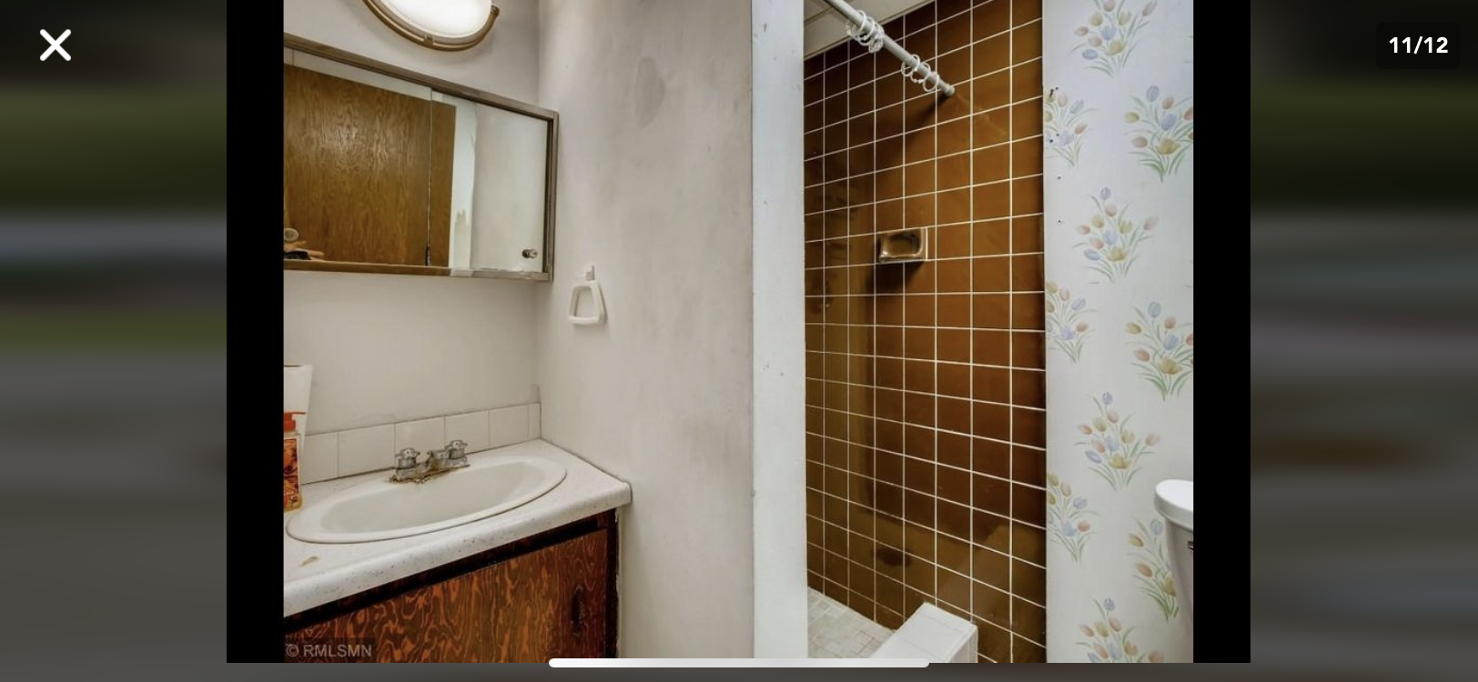Bathroom with a sink, mirror, and a brown tiled shower stall.