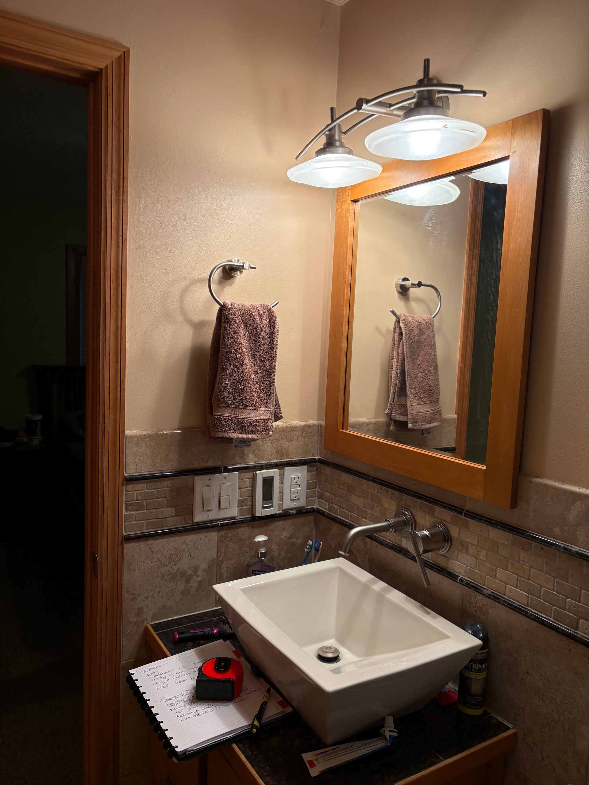 Bathroom with light fixture, mirror, sink, towel, and a measuring tape on counter.