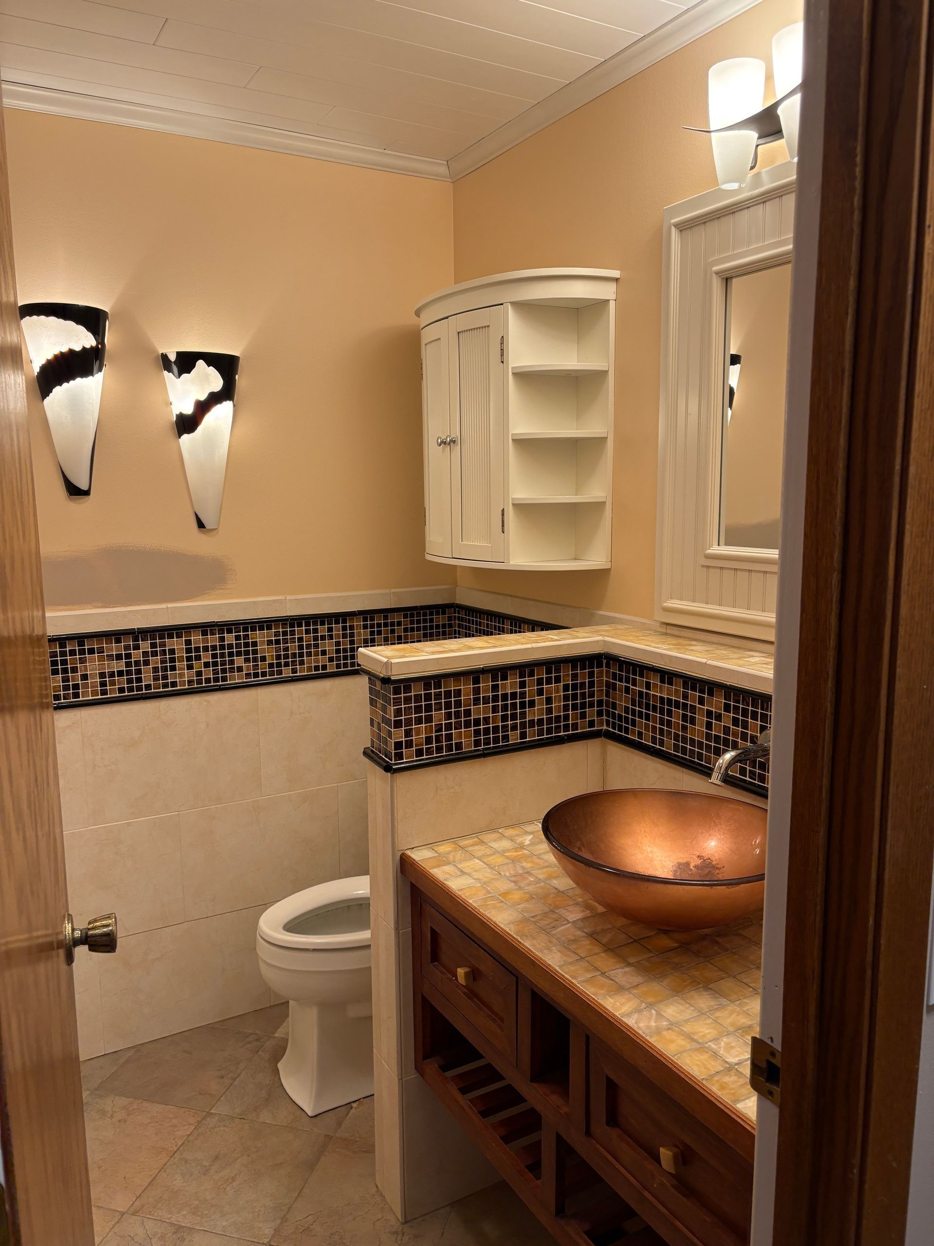 Bathroom with copper sink, mosaic tile, and decorative wall sconces.